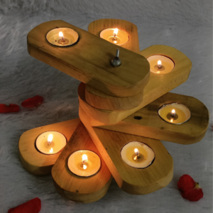 A tiered wooden candle holder with rotating arms holding lit tea lights, scattered with red rose petals on a soft white textured surface.